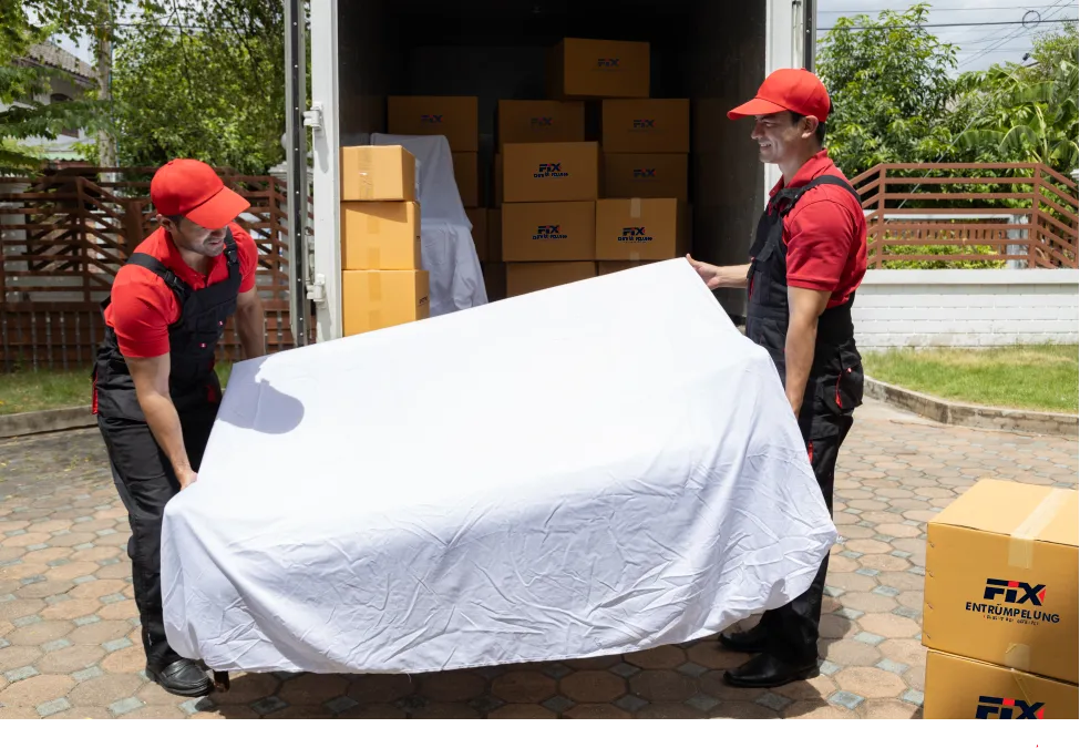 Zwei Mitarbeiter tragen ein abgedecktes Möbelstück in den Transporter